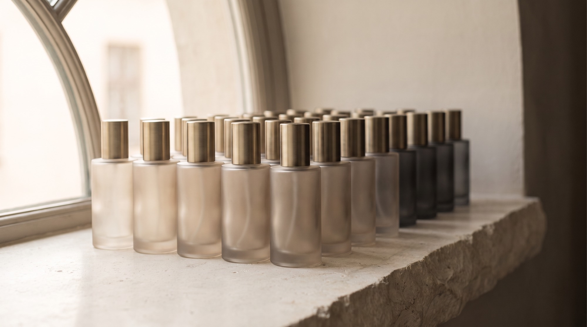 Rows of frosted glass bottles with brushed brass caps on a stone windowsill